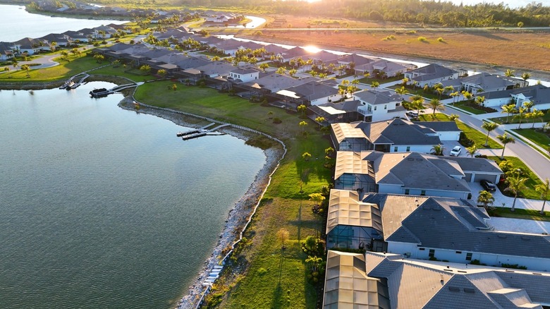 Aerial view of a waterfront Florida residential neighborhood with palm-lined streets, large homes, docks, and a lake reflecting the sunset