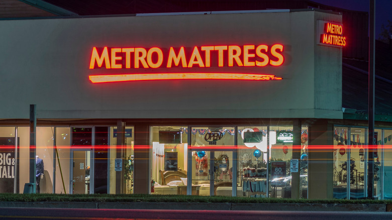 A nighttime view of Metro Mattress, sign and store interior glowing