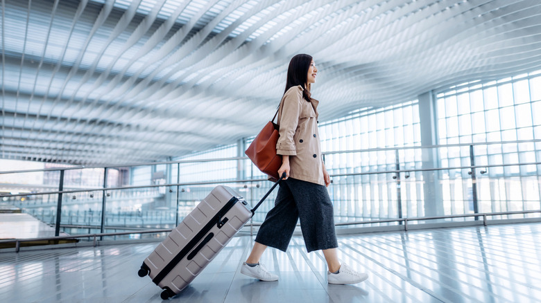 A smiling millennial woman walking with luggage at an airport.