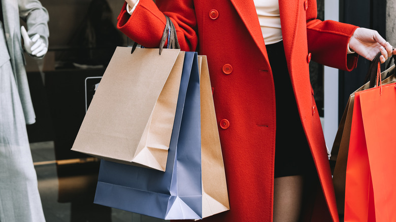 Midsection of a woman in a stylish red coat in a department store, carrying many bags
