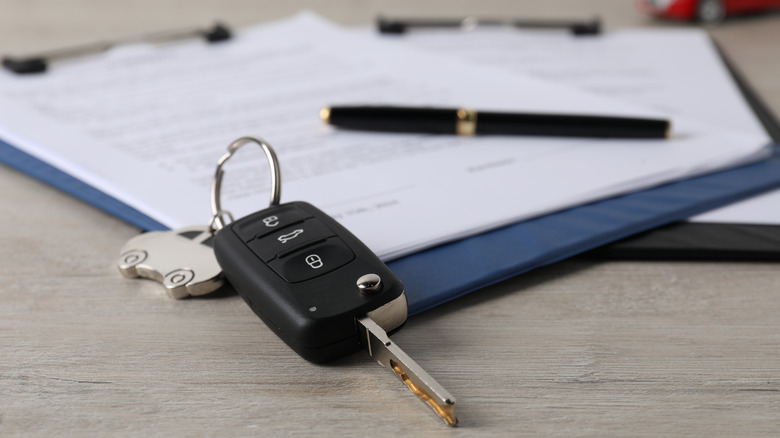 A car key propped up on a clip board with a contract on it and a pen in the background.