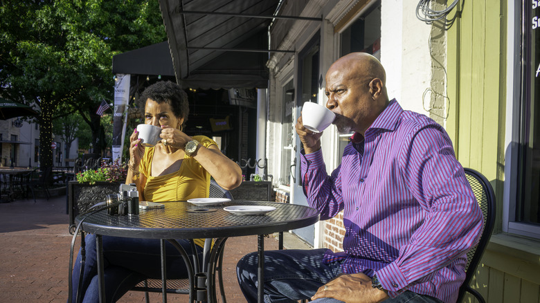 A mature couple sitting outside a cafe sipping coffee on a sunny day