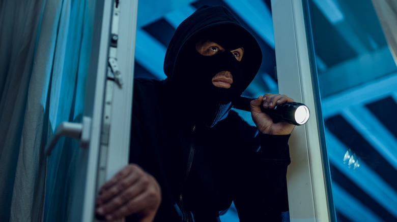 A masked man holding a flashlight while breaking into a house