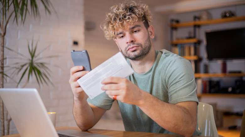 A Gen Z man looking at a pay stub while holding a calculator