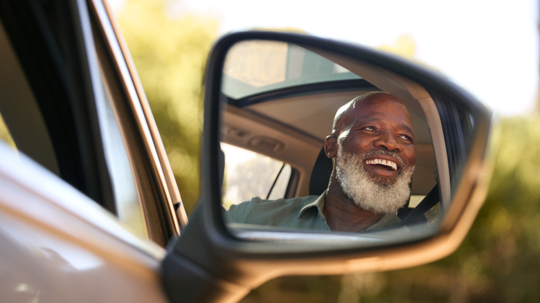 Car mirror reflecting older man in car.
