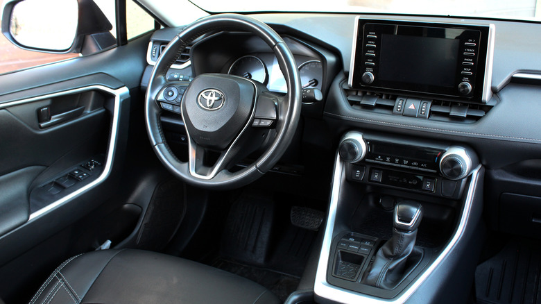 An interior view of a Toyota RAV4 with steering wheel, infotainment screen, and gear shifter visible.