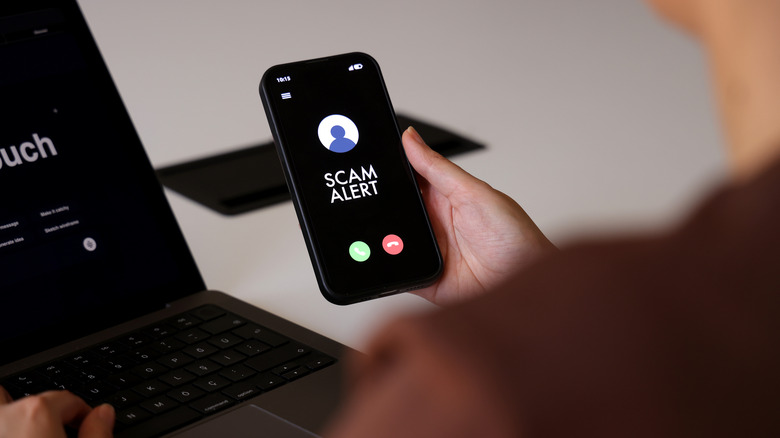 Person holding phone with a scam alert caller id.