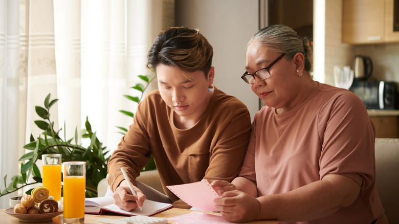 Younger man helping older woman at kitchen table