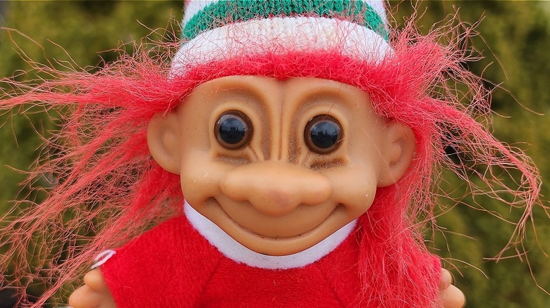 Troll doll wearing red sweater and green-and-white-striped hat while sitting outside