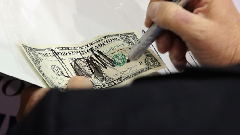 Trump signs a dollar bill for a supporter