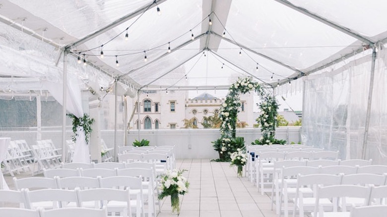 A rooftop wedding venue with floral arrangements and white chairs under a tent.