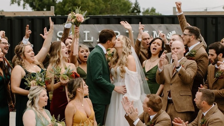 A bride and groom kissing while their wedding party cheers them on.
