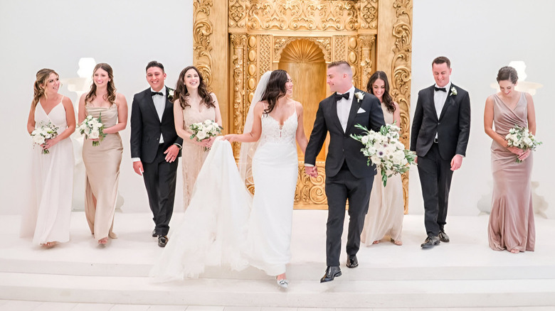 A bride and groom walking hand in hand with their wedding party behind them.