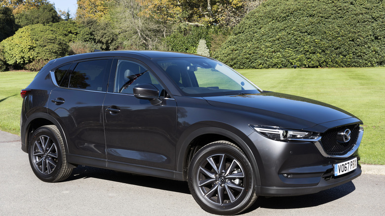 A Mazda CX-5 parked in front of a grassy field with trees in the background.