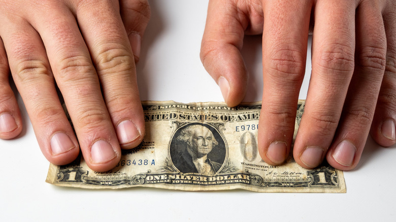 Hands stretching out a well-worn $1 bill across white table