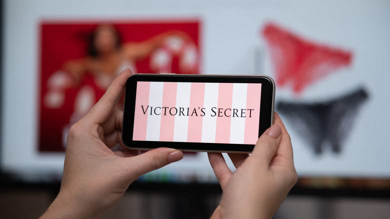 A woman's hands holding a cellphone with the Victoria's Secret logo onscreen