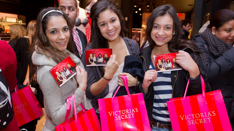 Three Gen Z women holding Victoria's Secret shopping bags in a mall