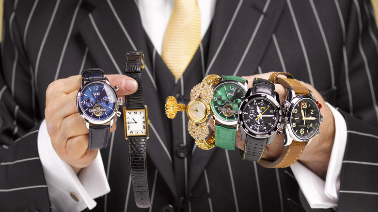 A man in a suit holding several expensive watches