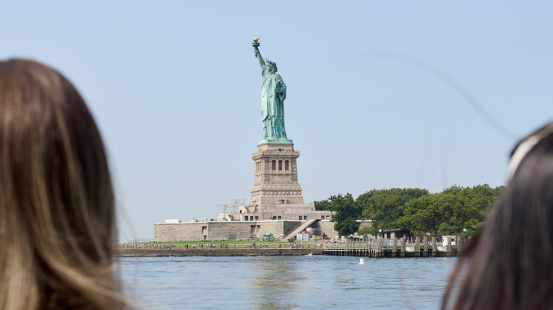 Two tourists admiring the Statue of Liberty from a ferry.