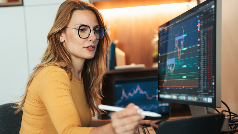 a light haired woman with black glasses checking the stock market on her home computer