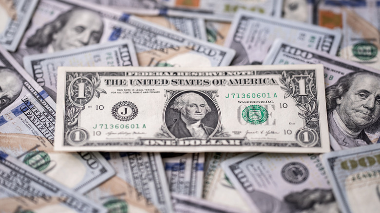 A $1 laying on top of a pile of $100 bills