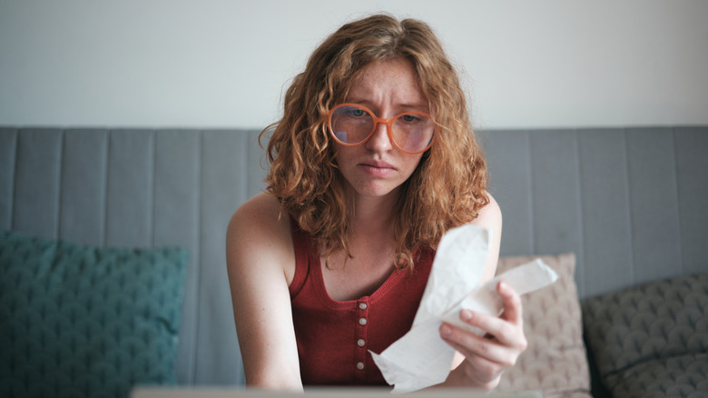 girl holding financial bills looking at laptop computer