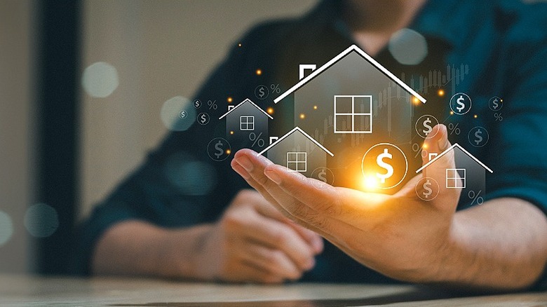Hand holding a digital projection of four houses with dollar signs