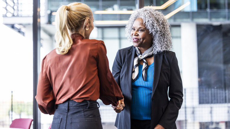 Two happy looking women in business attire shake hands