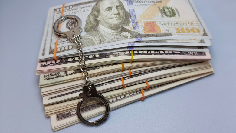 A pair of handcuffs resting atop a pile of $100 bills.