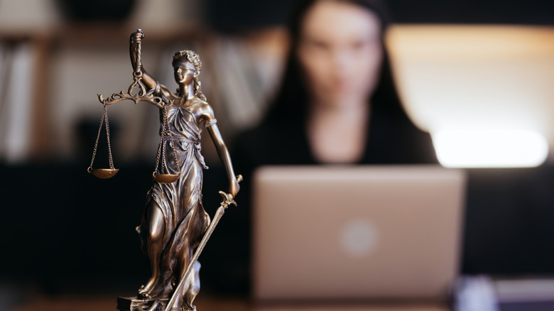 Statue of Justice with scales and a lawyer working on a laptop.