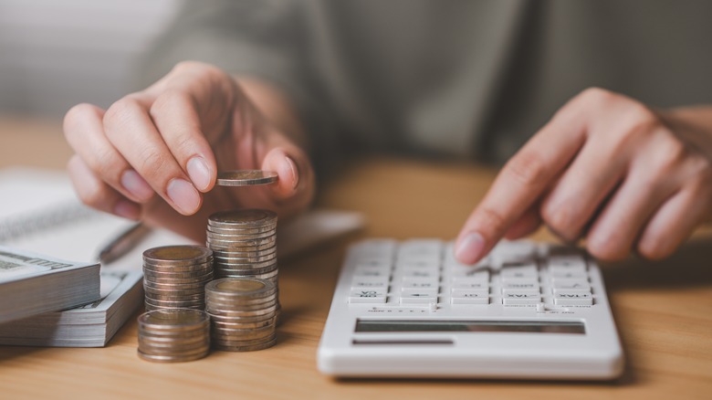 Person using calculator to count value of coin stack.