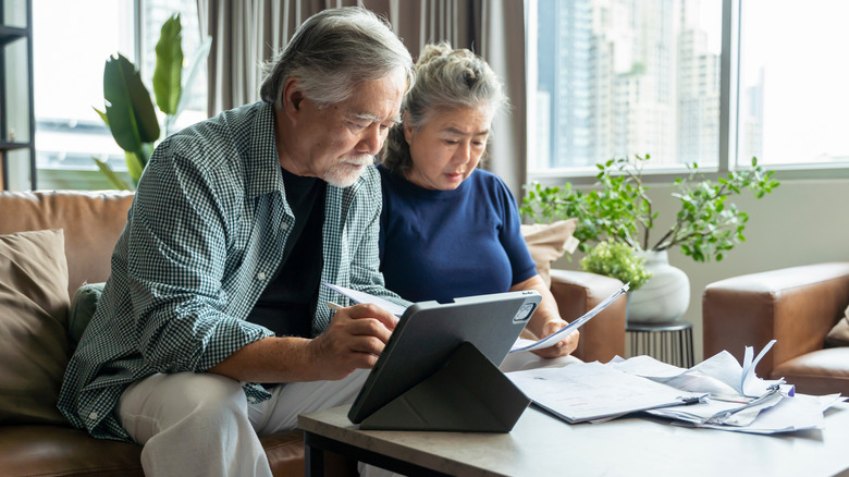 elderly Asian couple checking their bills on a tablet with papers on coffee table