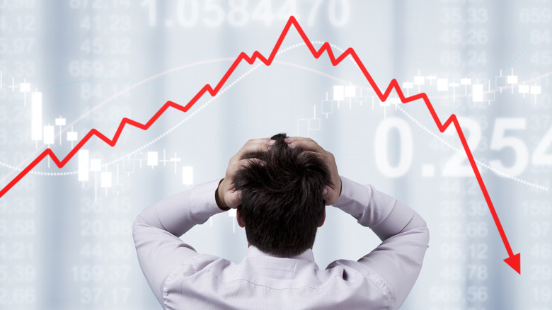 Business man with hands on head stands under red arrow pointing down representing an asset's decreasing value