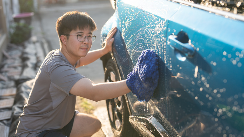 A young adult man washing car in yard with a wash cloth