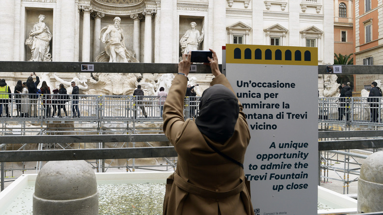 A tourist taking photos in front of the Trevi Fountain