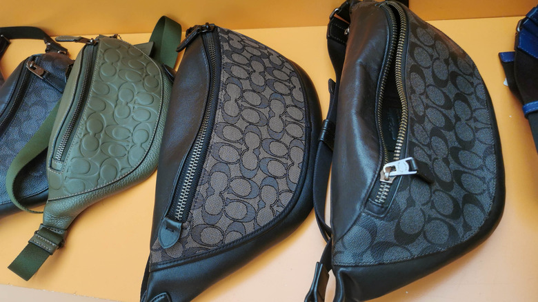 A row of Coach fanny packs against a yellow shelf