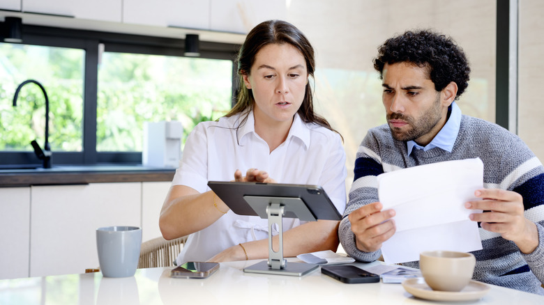 a couple sitting at their kitchen table with documents and a tablet and receipts around them