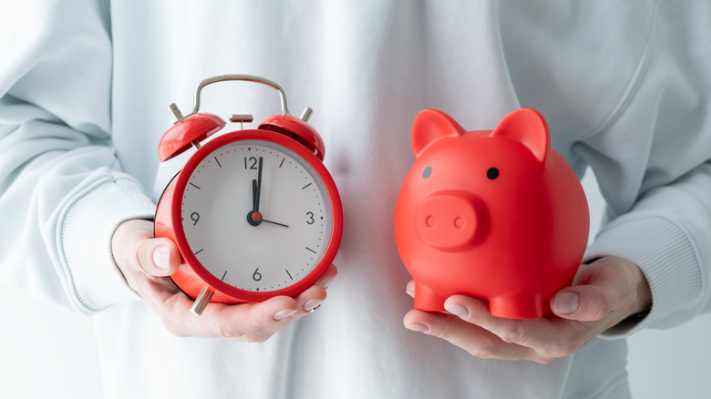 A person in a white shirt holding a clock and a piggy bank
