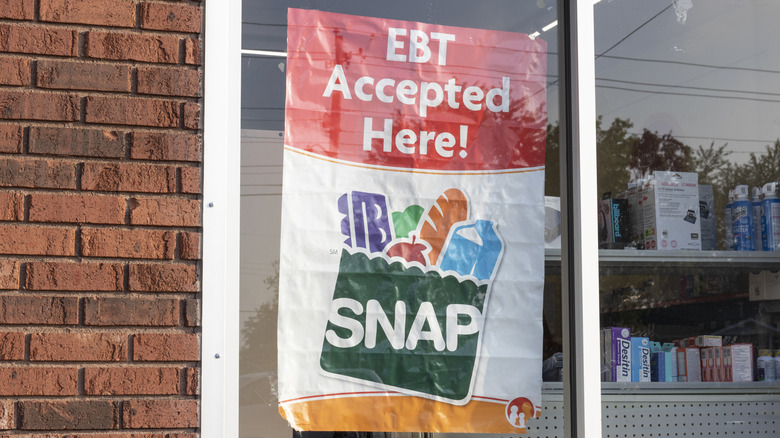 A SNAP-EBT sign on a store glass window, set in a brick storefront on a sunny day