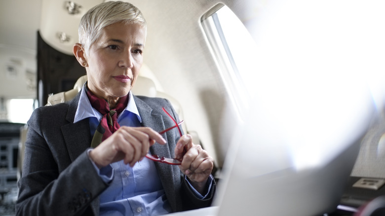 A senior woman seated on an airplane looking at her laptop screen