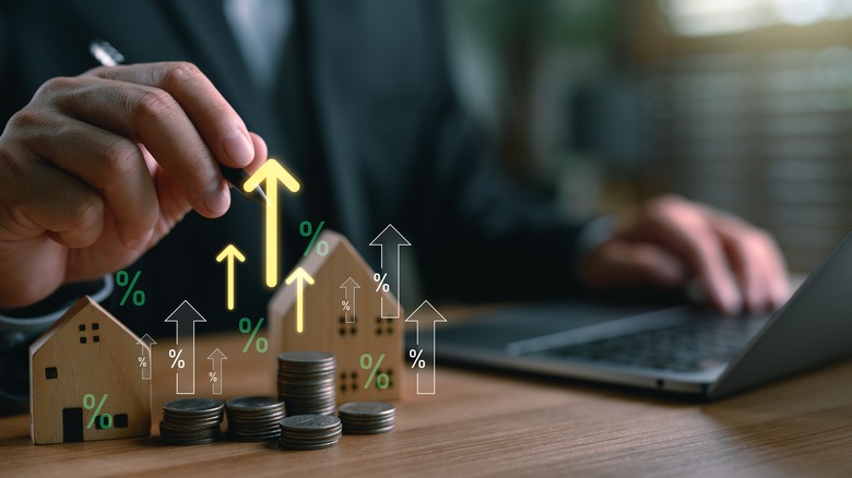 Man holding pen over wooden model of a home with arrows pointing upward.