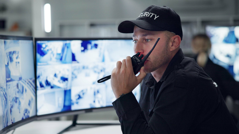 Private security guard speaking into a walkie talkie while looking at CCTV footage.