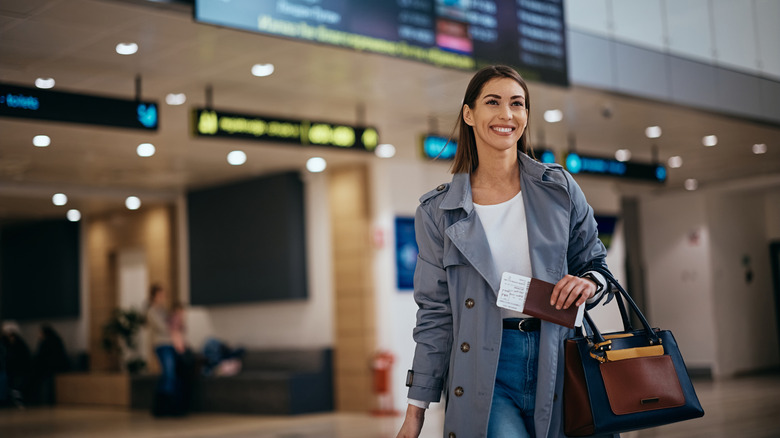 Happy woman walking through airport with ticket in hand