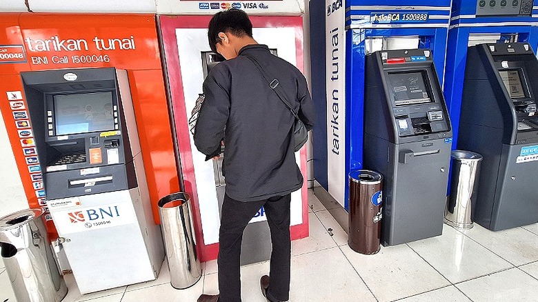 A man in a gray jacket standing in front of a line of ATMs in Indonesia