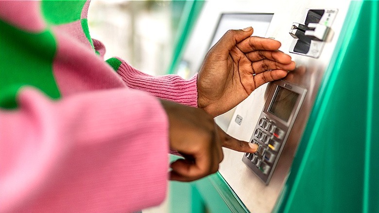 A woman in a green and pink sweater shielding an ATM keypad with her hand