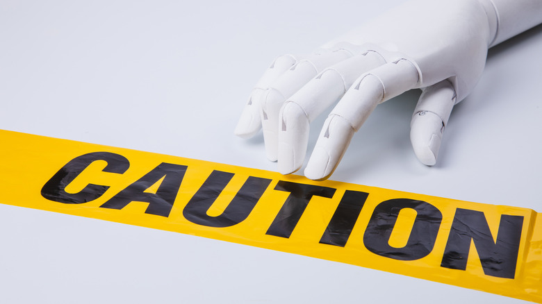Yellow tape reading caution by robotic hand