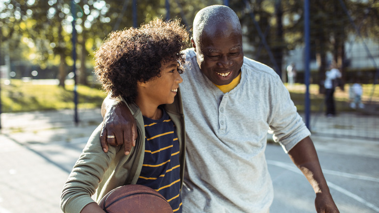 A smiling elderly man embraces his grandson on a basketball court