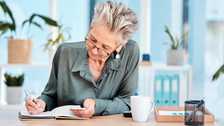 an older woman in a green blouse making notes at a desk