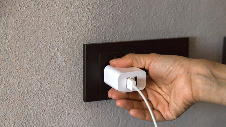 A person is plugging a white USB charger into a black wall socket