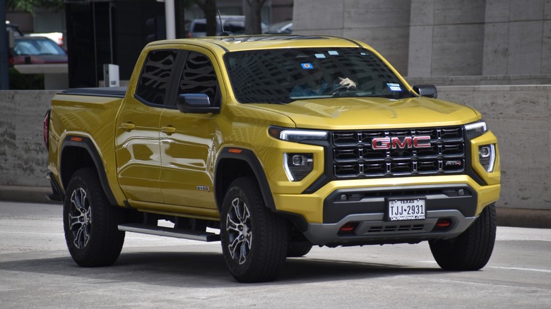 Yellow GMC Canyon AT4 pickup truck driving through a city street with a bold black grille and red GMC badge